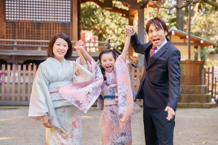 代々木八幡宮で七五三のご祈祷後にパパ、ママと一緒に楽しそうに手を繋ぐ7歳女の子の着物姿の写真
