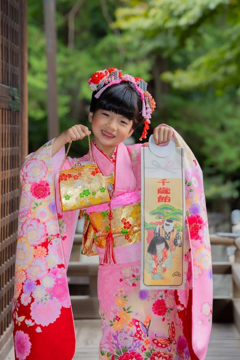代々木八幡宮の拝殿の回廊で千歳飴と和装バッグを持って笑顔の７歳着物姿の女の子の写真