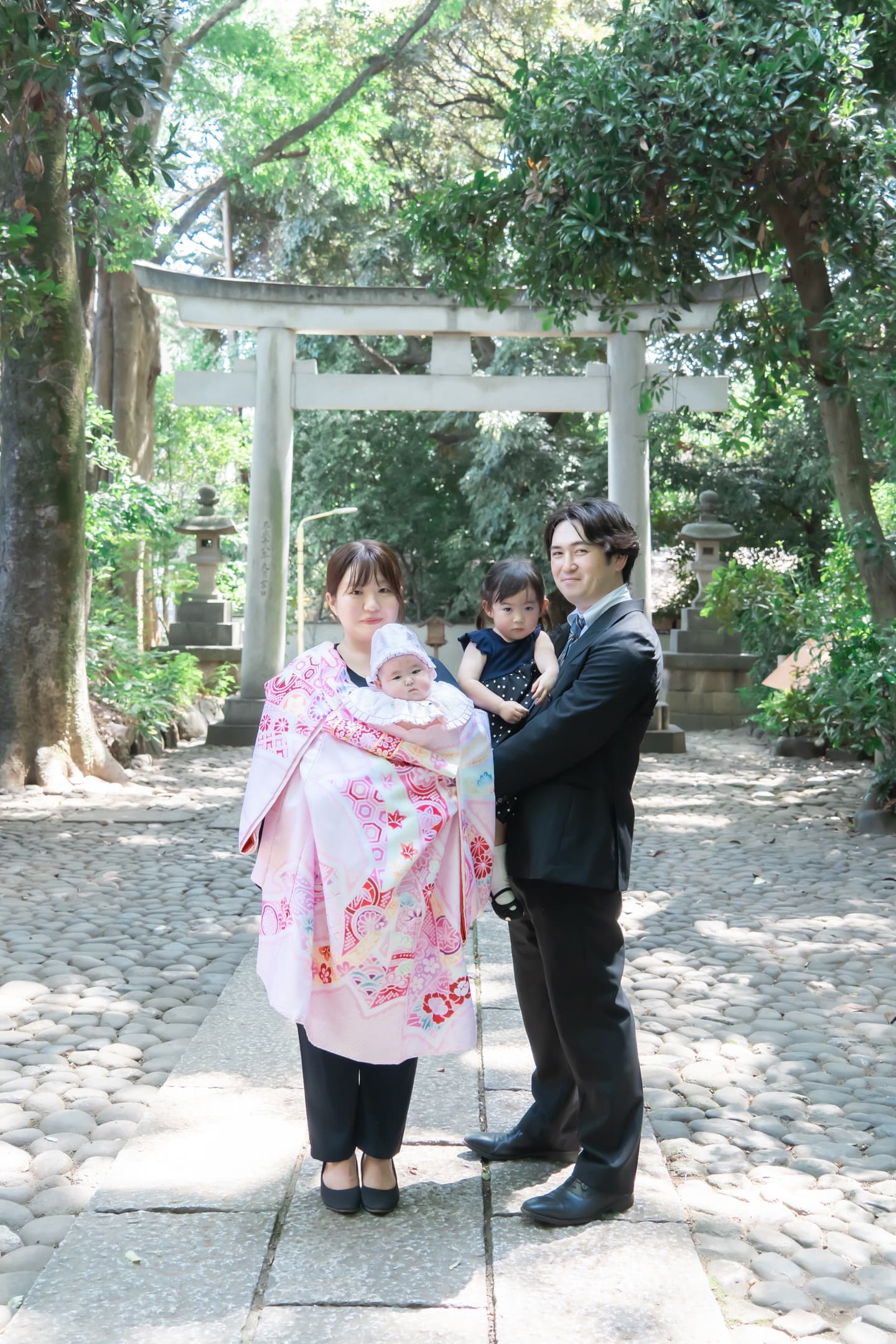 代々木八幡宮の参道の鳥居前でお宮参りの赤ちゃんを抱っこするご家族の写真｜美容室スプラッシュ