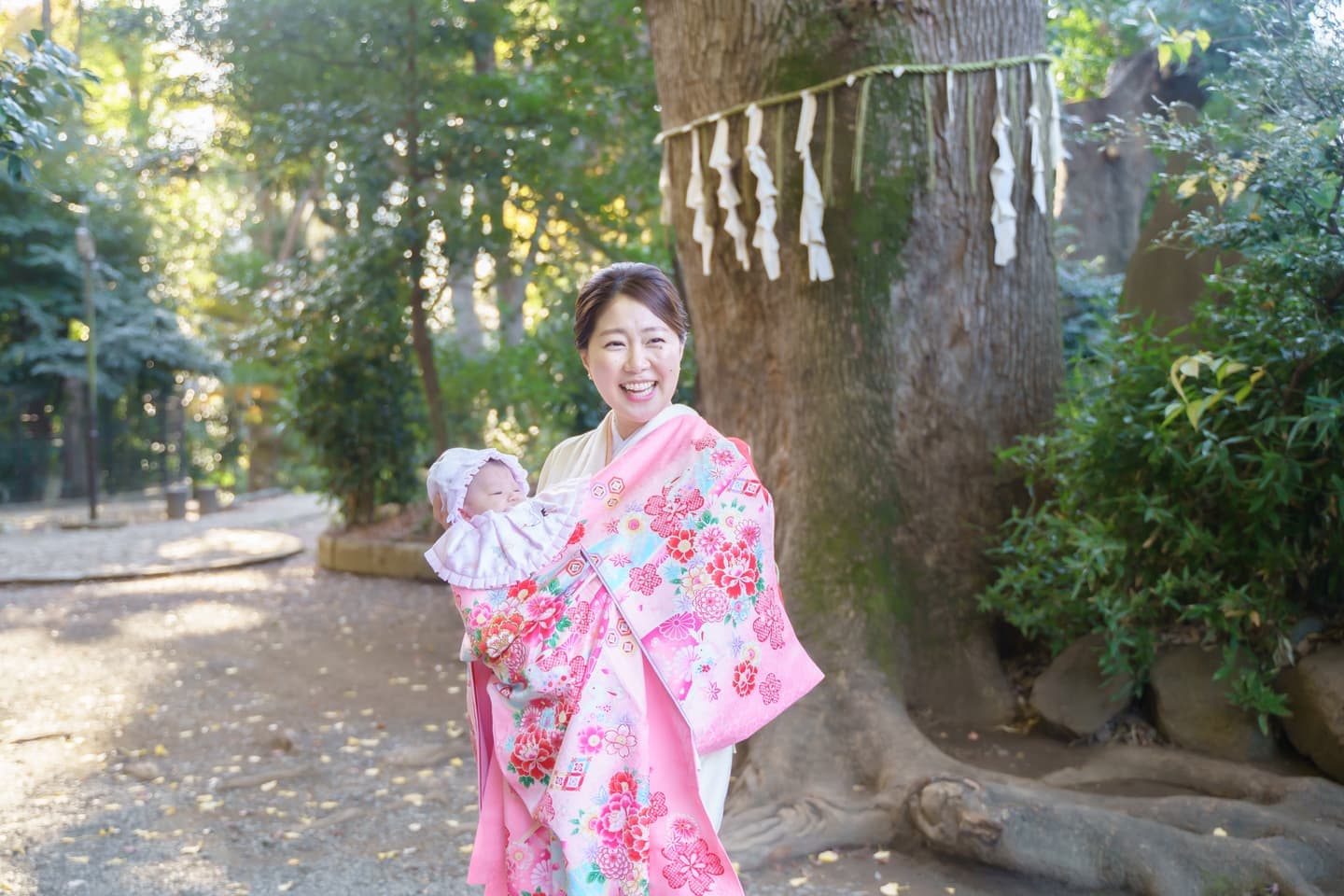 代々木八幡宮の御神木の前でお宮参りの赤ちゃんを抱っこして笑顔のママの写真｜美容室スプラッシュ