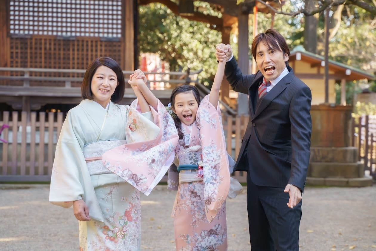代々木八幡宮で七五三のご祈祷後にパパ、ママと一緒に楽しそうに手を繋ぐ7歳女の子の着物姿の写真